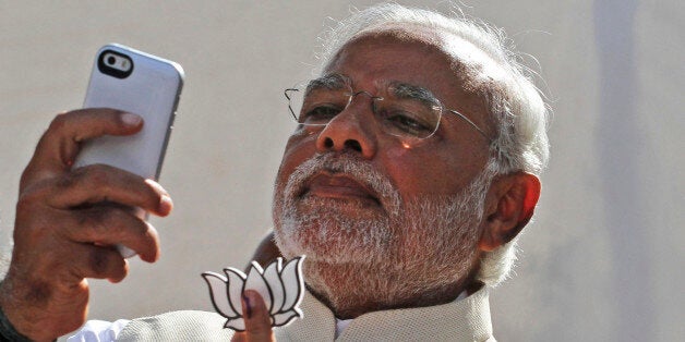 FILE- In this April 30, 2014 file photo, India's main opposition Bharatiya Janata Party's prime ministerial candidate Narendra Modi holds his party's symbol and looks into his phone after casting his vote in Ahmadabad, India. As India's Prime Minister Narendra Modi wraps up his first year on the job, one thing is clear, the prime minister understands the power of a good photograph. As the chief minister of the western state of Gujarat Modi managed the impossible _ being in many places at the same time. Using hundreds of thousands of dollars in equipment he dazzled voters by projecting a shockingly lifelike, three-dimensional holographic image of himself onto screens at election rallies in dozens of towns and villages. (AP Photo/Ajit Solanki, File)