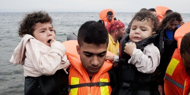 A refugee man carries children upon their arrival on Sykamia beach, west of the port of Mytilene, on the Greek island of Lesb