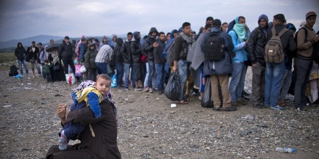 A Syrian woman changes her child's diaper as migrants and refugees queue at a camp to register after crossing the Greek-Maced