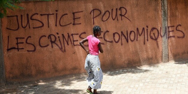 A woman walks past a wall with graffiti reading 'Justice for the economic crimes' in Ouagadougou on October 1, 2015. General Gilbert Diendere, the leader of Burkina Faso's short-lived coup, was in police custody on October 1, a security source told AFP. AFP PHOTO / SIA KAMBOU (Photo credit should read SIA KAMBOU/AFP/Getty Images)