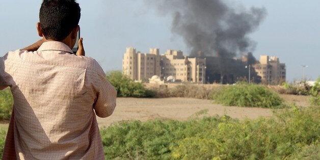 ADEN, YEMEN - OCTOBER 06: A man takes photo as smoke rises from al-Qasr Hotel hosting top Yemeni officials, after it was hit by rocket attack on October 06, 2015 in Aden, Yemen. At least 12 people were killed Tuesday in a rocket attack that targeted a hotel hosting top Yemeni officials in the southern city of Aden. (Photo by Wail Shaif Thabit/Anadolu Agency/Getty Images)