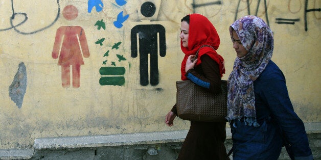 In this Tuesday, March 31, 2015 photo, Afghan university students walk past graffiti, in Kabul, Afghanistan. Farkhunda, a 27-