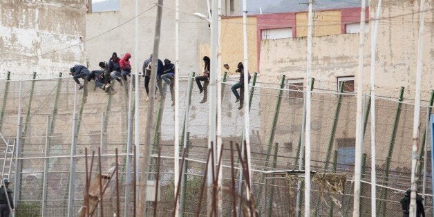 Would-be immigrants sit atop a border fence after attempting to cross from Morocco to the Spanish enclave of Melilla on Febru