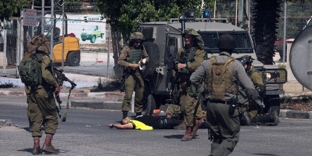 Israeli security forces stand next to the body of a Palestinian man who carried out a stabbing attack against an Israeli soldier at the entrance to the city of Hebron in the occupied West Bank on October 16, 2015. Israeli troops shot dead the Palestinian disguised as a news photographer who stabbed and wounded a soldier near the West Bank settlement of Kiryat Arba, the Israeli army said. AFP PHOTO / HAZEM BADER (Photo credit should read HAZEM BADER/AFP/Getty Images)