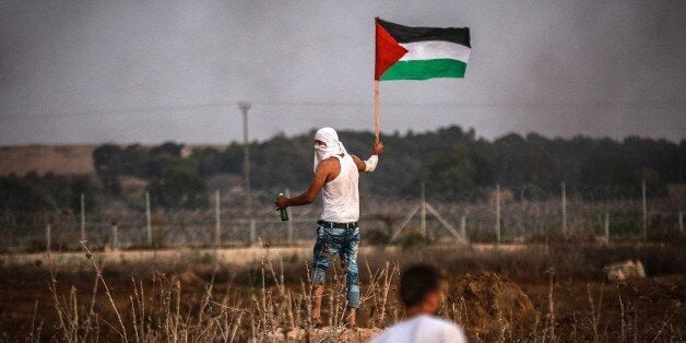 GAZA - OCTOBER 15: A Palestinian holds a Palestinian flag during clashes after Palestinians tried to attach Palestinian flag to the barbed wires on the Gaza border near Al-Bureij refugee camp, Gaza on October 15, 2015. (Photo by Ali Hassan/Anadolu Agency/Getty Images)