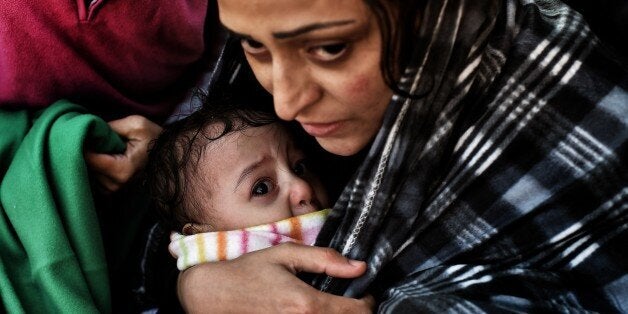 A woman holds her baby as fefugees and migrants arrive at the Greek island of Lesbos after crossing the Aegean sea from Turkey on September 30, 2015. UN Secretary-General Ban Ki-moon welcomed the European Union's decision to inject $1 billion to help countries overwhelmed by Syrian refugees, but said more must be done to relocate migrants. AFP PHOTO / ARIS MESSINIS (Photo credit should read ARIS MESSINIS/AFP/Getty Images)