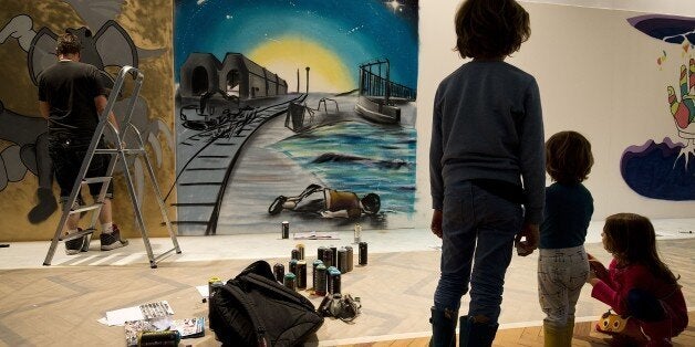 Children look at the art work 'Ni frontiere, ni souffrance' (No border, no pain) by French street artist MG La Bomba (unseen), depicting three-year-old Syrian boy Aylan Kurdi (bottom) who drowned while fleeing the war in Syria, as part of the 'Twelve hours to change the gaze' event at the French national Immigration museum in Paris, on September 12, 2015. AFP PHOTO / JOEL SAGET ==RESTRICTED TO EDITORIAL USE, MANDATORY MENTION OF THE ARTIST UPON PUBLICATION, TO ILLUSTRATE THE EVENT AS SPECIFIED IN THE CAPTION == (Photo credit should read JOEL SAGET/AFP/Getty Images)