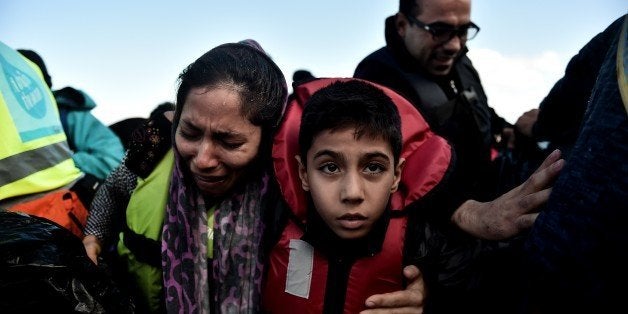 A woman, holding her child, cries as she arrives, with other refugees and migrants on the Greek island of Lesbos on October 25, 2015 after they crossed the Aegean sea from Turkey. At least three migrants -- two children and a woman -- drowned when their boat sank off the Greek island of Lesbos, the coastguard said, the latest fatalities in Europe's refugee crisis. Around a dozen others, mostly Afghans, are still missing after the rickety vessel, carrying 60 people, went down at dawn as it made the perilous crossing from Turkey, according to the Greek coastguard. AFP PHOTO / ARIS MESSINIS (Photo credit should read ARIS MESSINIS/AFP/Getty Images)