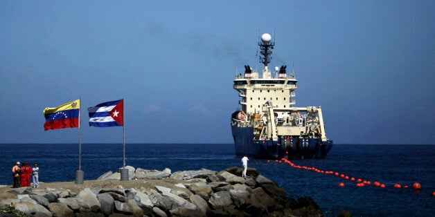 FILE - In this Jan. 22, 2011 file photo, people stand on a breakwater, with a Venezuelan flag, left, and a Cuban flag, as a specialized ship rolls out a fiber-optic cable, suspended from buoys, off La Guaira, Venezuelan coast. Cuban officials last year welcomed the arrival of the undersea fiber-optic cable linking the country to Venezuela, which was supposed to boost web capacity 3,000-fold. Even a retired Fidel Castro had hailed the dawn of a new cyber-age on the island. More than a year later, the government barely speaks of the cable anymore and Cuba's internet connection is still the slowest in the hemisphere. (AP Photo/Ariana Cubillos, File)