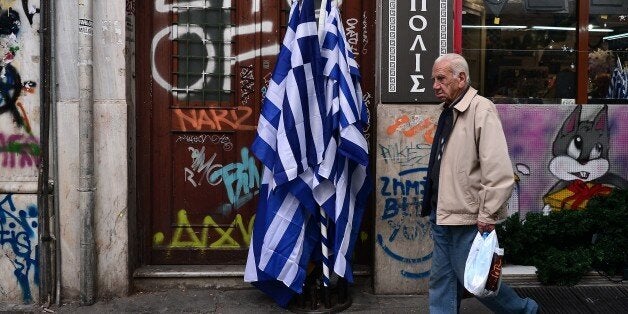 An elderly man walks past Greek flags on sale in central Athens, on October 29, 2015. The government is under increased pressure to submit two new draft bills to Greek Parliament in order to receive the 2-billion-euro tranche of its bailout plan. AFP PHOTO / LOUISA GOULIAMAKI (Photo credit should read LOUISA GOULIAMAKI/AFP/Getty Images)