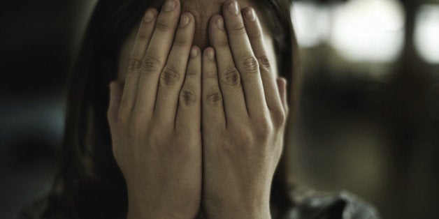 A young woman looking anxious and fearful with her hands over her eyes