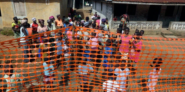 In this photo taken Friday, Aug. 14, 2015, people wait to be released from Ebola quarantine by Sierra Leone President Ernest Bai Koroma in the village of Massessehbeh on the outskirts of Freetown, Sierra Leone. Five months after a man traveled to his home village for festivities marking the end of Ramadan, and died suddenly from Ebola, but now President Koroma came to cut down the fencing to mark the formal end of Sierra Leone's largest remaining Ebola quarantine.(AP Photo/Sunday Alamba)
