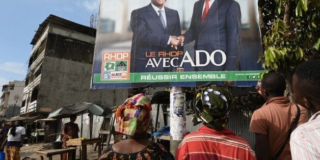 Two women look at a campaign poster that reads, 'The RHDP is with the ADO togther we can succeed' ('ADO' for Alassane Dramane Ouattara) presenting the candidates of the Rally of Houphouetists for Democracy and Peace (RHDP) Ivorian President Alassane Ouattara (ADO) (R) and Albert Toikeusse Mabri of the Union President for Democracy and Peace in Cote d'Ivoire (UDPCI) on October 9, 2015 in Kumasi, a popular district of Abidjan. Ivory Coast's presidential election will take place in a 'peaceful climate', President Alassane Ouattara in Abidjan, ahead of October 25 polls seen to be crucial for stability after a decade of political and military crisis. AFP PHOTO / SIA KAMBOU (Photo credit should read SIA KAMBOU/AFP/Getty Images)