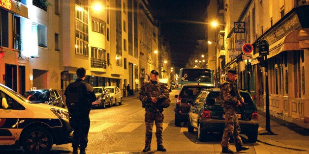 French soldiers and a police officer stand on a street next to Rue de Charonne, in Paris, Saturday, Nov. 14, 2015. The sidewa