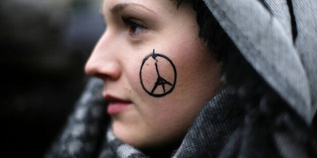 A woman has a peace sign combined with the Eiffel Tower painted on her face as she arrives for a minute of silence for the victims of Friday's attacks in Paris, in front of the French Embassy in Berlin, Sunday, Nov. 15, 2015. Multiple attacks across Paris on Friday night have left scores dead and hundreds injured. (AP Photo/Markus Schreiber)