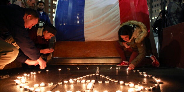 Stephane Fosik, from left, Cedrine Plongeur and Cloe Tinchant light candles in the shape of a peace symbol in LOVE Park, Saturday, Nov. 14, 2015, during a candlelight vigil to remember the victims of the attacks in Paris. (AP Photo/Joseph Kaczmarek)