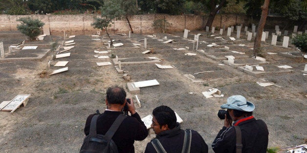 Pakistani news photographers take pictures of desecrated graves at the minority Ahmadi sect graveyard in Lahore on December 3