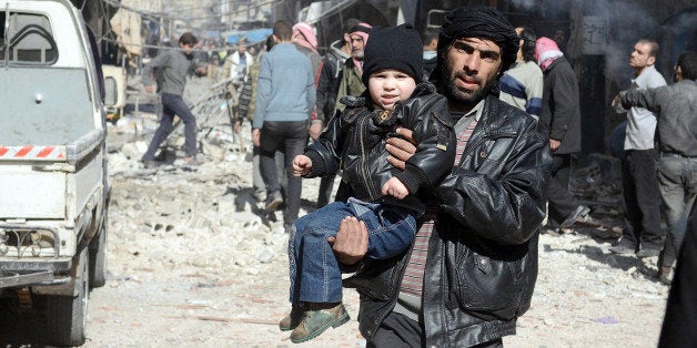 DOUMA, SYRIA - FEBRUARY 02: A Syrian man takes his son away after Syrian regime's air forces' air attack on East Ghouta region with 'Vacuum Bomb' that killed at least 10 people and injured 75 others in Douma, Syria on February 02, 2015. (Photo by Yousef Albostany/Anadolu Agency/Getty Images)