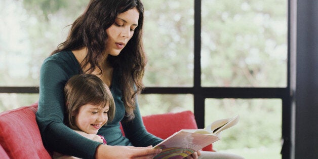 Mother and daughter (2-4) sitting on sofa, reading book