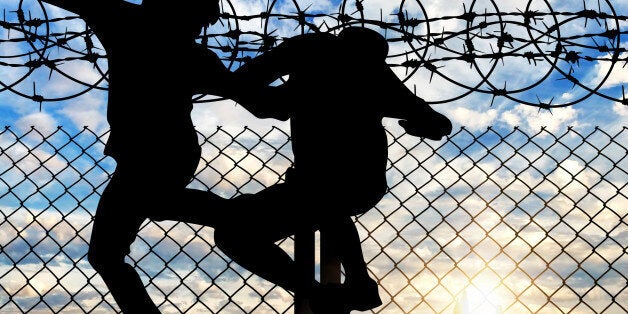 Concept of the refugees. Silhouette of refugees crossing the fence with barbed wire against the evening sky and the city in t