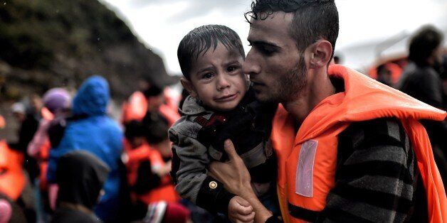 A man holds a young boy after they arrived with other refugees and migrants on the Greek island of Lesbos after crossing the Aegean sea from Turkey on October 21, 2015. An EU scheme to relocate asylum seekers from overstretched Italy and Greece could grind to a halt just two weeks after it began if member states fail to meet their obligations, an EU source said on October 21. AFP PHOTO / ARIS MESSINIS (Photo credit should read ARIS MESSINIS/AFP/Getty Images)