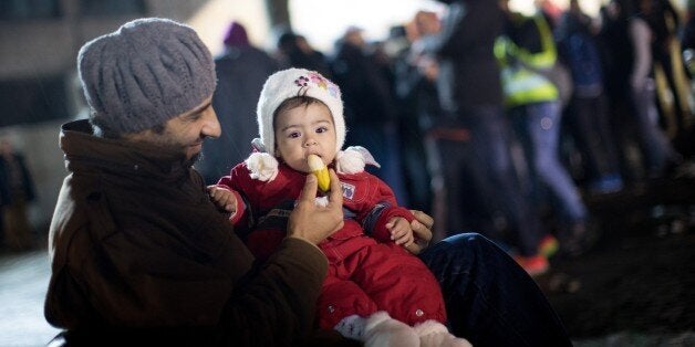 A man from Syria feeds his daughter as asylum seekers line up in front of the State Office of Health and Social Affairs (LAGeSo) registration centre in Berlin on December 21, 2015. / AFP / dpa / Kay Nietfeld / Germany OUT (Photo credit should read KAY NIETFELD/AFP/Getty Images)