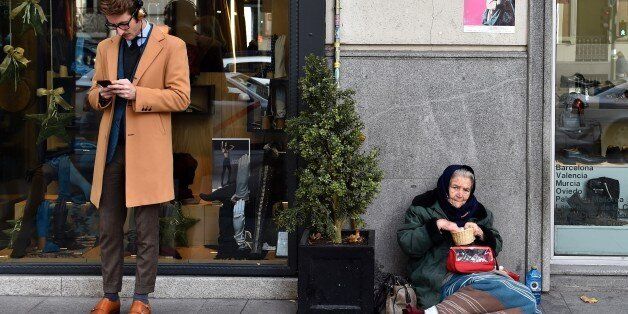 A man consults a mobile phone beside a woman begging on the pavement outside a clothes store in Salamanca an upscale neighbourhood of Madrid on December 15, 2015. The number of millionaires in Spain -- defined as having a fortune of over a million US dollars excluding their main residence and consumer goods -- rose by 40 percent to 178,000 last year from 2008 when the crisis started, according to consulting firm Capgemini. At the same time the number of people living with 'severe material deprivation' in the country has doubled since 2007 to just over three million last year, according to a study by anti-poverty agency Oxfam. AFP PHOTO/ GERARD JULIEN / AFP / GERARD JULIEN (Photo credit should read GERARD JULIEN/AFP/Getty Images)