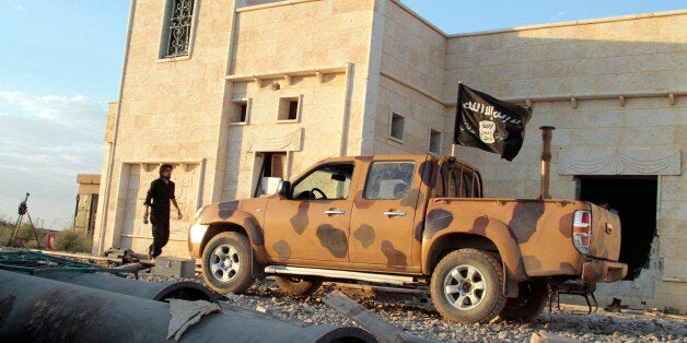 An opposition fighter walks near a vehicle flying a black Jihadist flag with Islamic writing on it proclaiming in Arabic that 'There is no God but God and Mohammed is the prophet of God' in the northern rebel-held Syrian city of Raqqa on October 6, 2013. UN-Arab League peace envoy Lakhdar Brahimi urged Syria's warring parties to hold talks 'without preconditions' and said he hoped negotiations could take place in Geneva in late November. AFP PHOTO/MOHAMMED ABDEL AZIZ (Photo credit should read MOHAMMED ABDUL AZIZ/AFP/Getty Images)