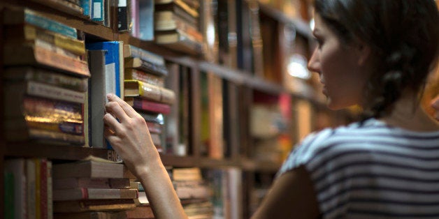 Beautiful woman looking at books in a library. Ambient light to emphasize the mood and location. Converted from RAW.