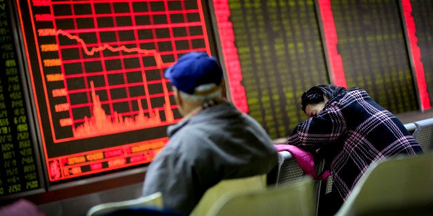 A woman takes a nap as a man looks at an electronic board displaying stock prices at a brokerage house in Beijing, Monday, Ja