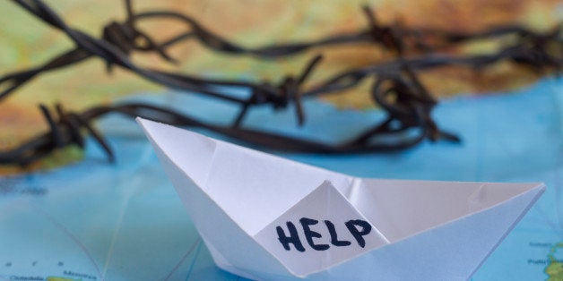 White paper boat onto world map with 'Help' sign on it and barbed wire.