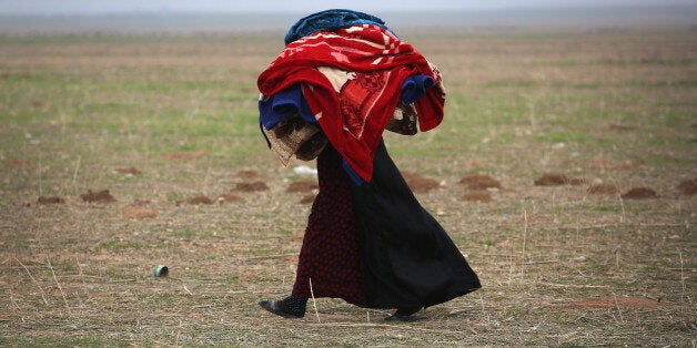 SINJAR, IRAQ - NOVEMBER 16: A woman carries blankets into a Kurdish-controlled area after fleeing her ISIL or Daesh-held frontline town on November 16, 2015 to Sinjar, Iraq. Peshmerga forces carefully screened the displaced Iraqis as they arrived, fearing enemy infiltrators and suicide bombers. Kurdish forces, with the aid of massive U.S.-led coalition airstrikes, liberated Sinjar from ISIL extremists, known in Arabic as Daesh, moving the frontline south. About a thousand villagers in Ghabosyeh fled north to Kurdish held territory, to take refuge camps or onward as refugees to Turkey or Europe. (Photo by John Moore/Getty Images)