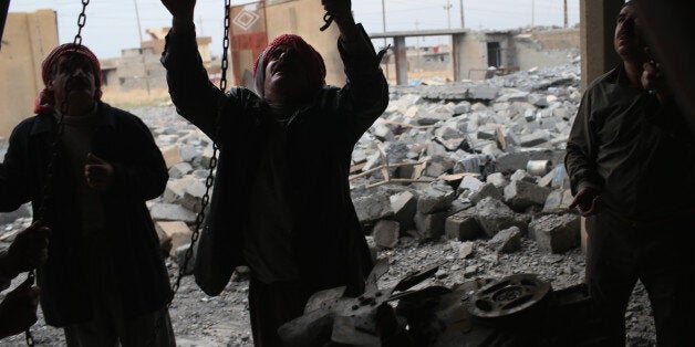 SINJAR, IRAQ - NOVEMBER 16: Yazidis work to lift an engine to salvage it from the rubble of an auto repair shop destroyed by an airstrike on November 16, 2015 in Sinjar, Iraq. Kurdish forces, with the aid of months of U.S.-led coalition airstrikes, liberated the town from ISIL extremists, known in Arabic as Daesh, in recent days. Although the battle was deemed a major victory, much of the city lay in complete ruins. (Photo by John Moore/Getty Images)