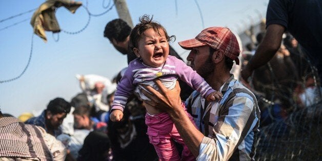 A Syrian man fleeing the war carries a child over border fences to enter Turkish territory illegally, near the Turkish border crossing at Akcakale in Sanliurfa province on June 14, 2015. Turkey said it was taking measures to limit the flow of Syrian refugees onto its territory after an influx of thousands more over the last days due to fighting between Kurds and jihadists. Under an 'open-door' policy, Turkey has taken in 1.8 million Syrian refugees since the conflict in Syria erupted in 2011. / AFP / BULENT KILIC (Photo credit should read BULENT KILIC/AFP/Getty Images)