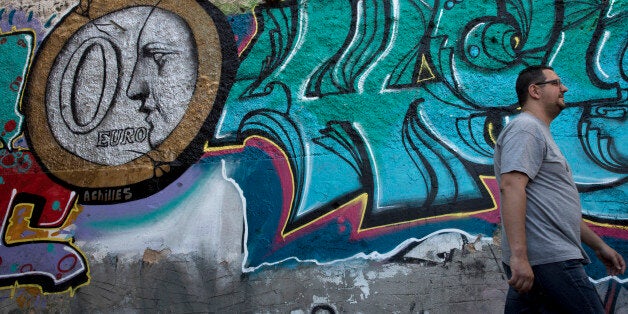 In this photo made on Saturday, June 20, 2015, a man walks past graffiti titled "0 Euro" by street Artist Achilles in Athens.