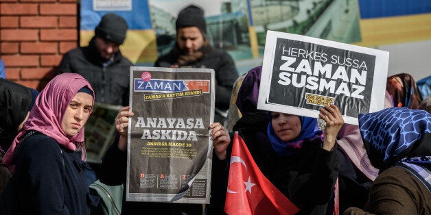 A Zaman supporter holds the latest edition of Turkish daily newspaper Zaman with the headline 'Suspended the constitution' while another holds a placard reading 'Zaman won`t be silent' in front of the newspaper's headquarters in Istanbul on March 5, 2016, after Turkish authorities seized the headquarters in a midnight raid. Turkish authorities on March 5 were in control of the newspaper staunchly opposed to President Recep Tayyip Erdogan after using tear gas and water cannon to seize its headquarters in a dramatic raid that raised fresh alarm over declining media freedoms. Police fired the tear gas and water cannon just before midnight at a hundreds-strong crowd that had formed outside the headquarters of the Zaman daily in Istanbul following a court order issued earlier in the day. / AFP / OZAN KOSE (Photo credit should read OZAN KOSE/AFP/Getty Images)