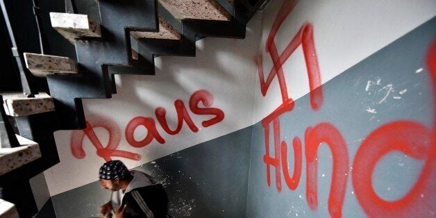 A migrant walks the stairway in a refugee housing block in Waltrop, western Germany, painted with a swastika graffiti and a writing "get out dogs," Tuesday, Oct. 13, 2015. Unknown persons sprayed extremist anti refugee graffiti on and in several refugee homes in the city the night before. (AP Photo/Martin Meissner)