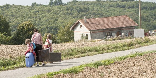 Mother and children wandering through countryside, dragging suitcases behind them
