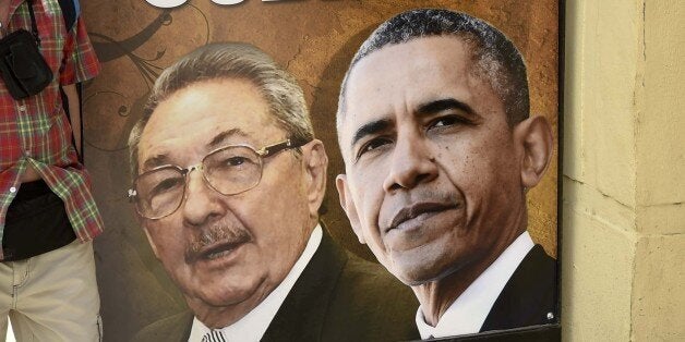 A tourist poses for a picture with a sign placed at the entrance of a restaurant with the images of Cuban and US Presidents R