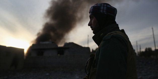 SINJAR, IRAQ - NOVEMBER 15: A Kurdish Peshmerga soldier passes by tires set afire days before by ISIL extremists to hinder airstrikes on November 15, 2015 in Sinjar, Iraq. Kurdish forces, with the aid of months of U.S.-led coalition airstrikes, liberated the town from ISIL extremists, known in Arabic as Daesh, in recent days. Although many minority Yazidis celebrated the victory, their home city of Sinjar lay in complete ruins. Local Yazidi fighters who fought with Kurdish forces and some former residents have been taking any salvagable items out of the rubble, the town being uninhabitable and perilously close to the frontline. (Photo by John Moore/Getty Images)