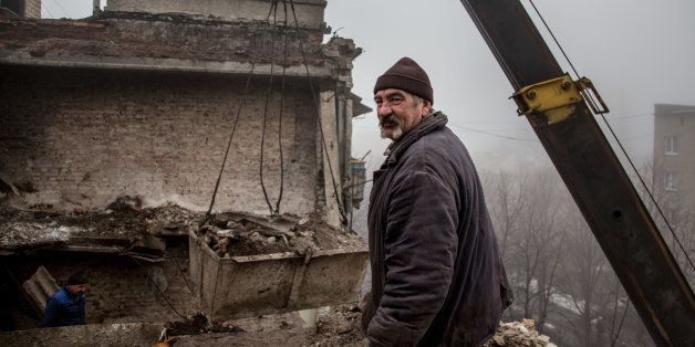 In this photo taken on Wednesday, Feb. 3, 2016, a construction worker removes rubble from the roof of a severely damaged condo in Debaltseve, eastern Ukraine. Money from Russia helps to the rebuild eastern Ukrainian town of Debaltseve, a strategic rail hub that rebels pounded for weeks before driving out the government troops a year ago. But there has been little or no money to spare for the nearby villages, which still bear the scars of one of the fiercest battles of the war. (AP Photo/Petr Anikukhin)