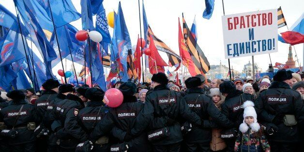 Police officers stand guard during a rally to celebrate the second anniversary of Russia's annexation of Crimea just off Red Square in Moscow, Russia, Friday, March 18, 2016. Russia annexed Crimea in 2014 after a hastily organized referendum not recognized by the United States and the European Union. A poster reads Fraternity and Unity. (AP Photo/Ivan Sekretarev)