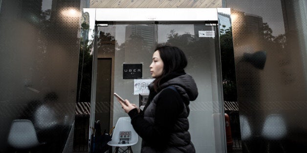 A woman walks past the Uber offices in Hong Kong on January 22, 2016. Two Hong Kong Uber drivers were fined on January 22 after pleading guilty to driving without proper licences, the latest slap on the wrist for the global ride-sharing giant. AFP PHOTO / Philippe Lopez / AFP / PHILIPPE LOPEZ (Photo credit should read PHILIPPE LOPEZ/AFP/Getty Images)