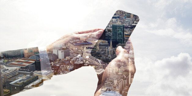 Double exposure of a business man using a smart phone with a view of the city of London and the sky.