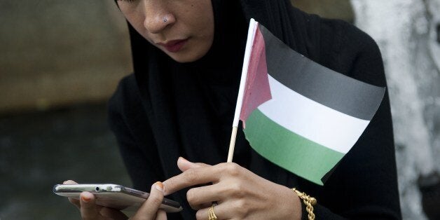 A protestor check her phone as she holds a Palestinian flag outside the Israeli embassy in Bangkok, during a demonstration against Israeli air strikes on Gaza, on July 15, 2014. Israel pressed its campaign of punishing raids on Gaza, and the Palestinian death toll rose to 172, with another 1,230 wounded. AFP PHOTO/ Nicolas ASFOURI (Photo credit should read NICOLAS ASFOURI/AFP/Getty Images)