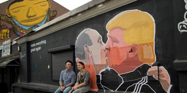 A couple sits in front of graffiti depicting Russian President Vladimir Putin, left, and Republican presidential candidate Do