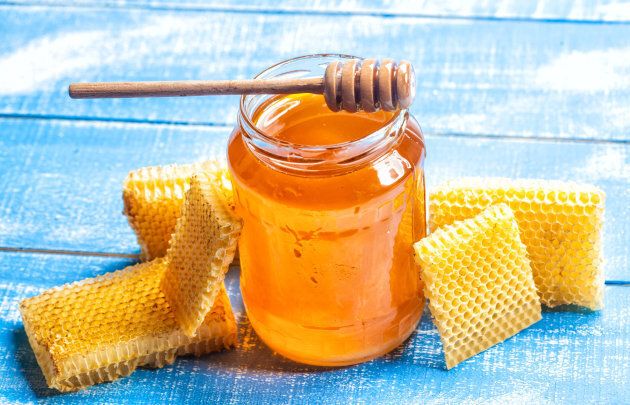 jar of honey with wooden honey dipper and honeycomb on white