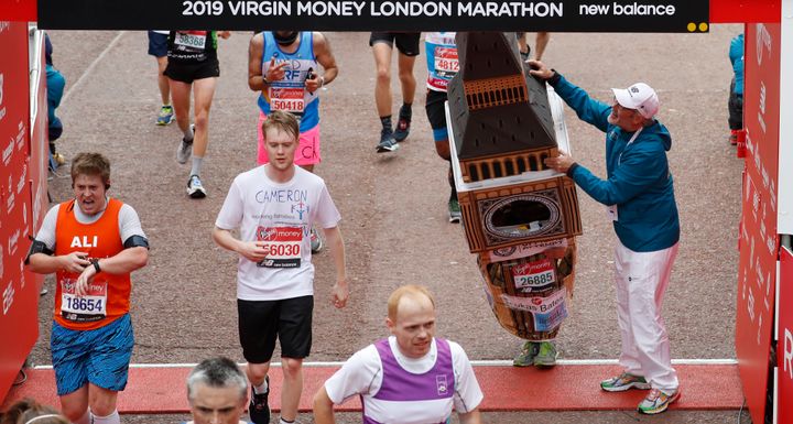 Lukas Bates wearing a costume of the Queen Elizabeth Tower - known as Big Ben - is helped by an official as he attempts to get past the finishing line, during the 39th London Marathon.