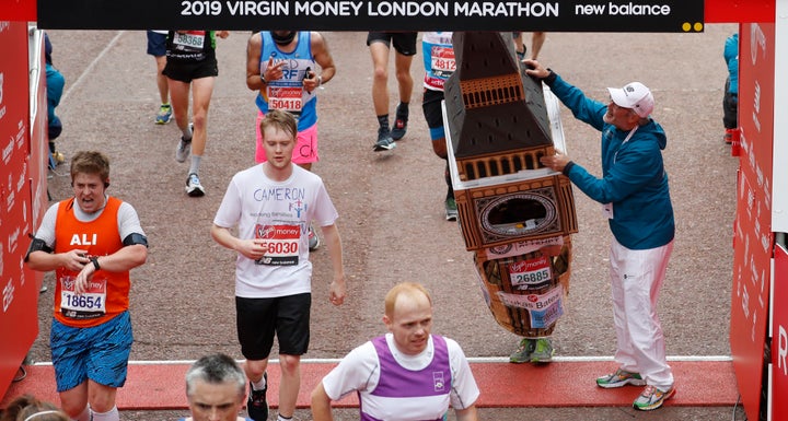 Lukas Bates wearing a costume of the Queen Elizabeth Tower - known as Big Ben - is helped by an official as he attempts to get past the finishing line, during the 39th London Marathon.