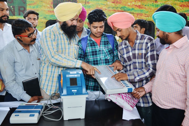 Indian electoral officials demonstrate how to use an Electronic Voting Machine (EVM) and Voter-Verified Paper Audit Trail (VVPAT) to passengers during a voter awareness programme.